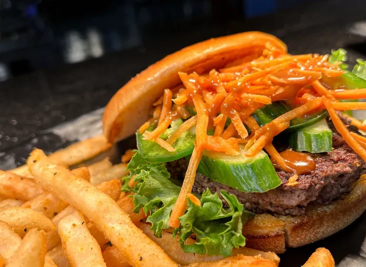 A hamburger topped with cucumbers, jalapenos, thin cut carrots, and topped with a peanut sauce.