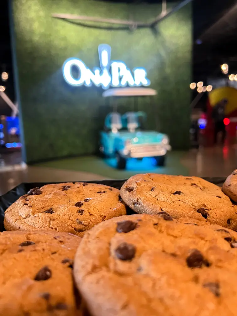 A plate of chocolate chip cookies, in the far background is the On Par logo and selfie wall.