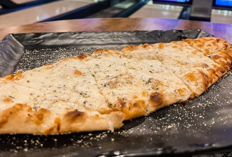 A plate of flatbread topped with cheese, garlic, and seasoning.
