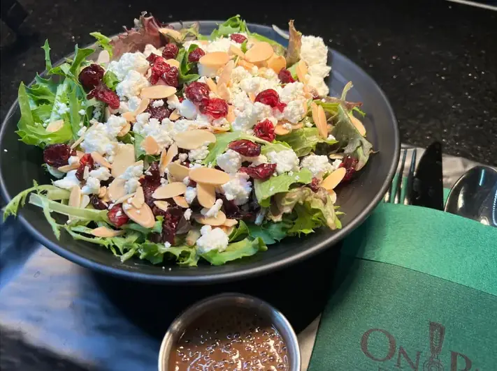 A salad bowl filled with spring mix, topped with goat cheese, pine nuts, dried cranberries, and serviced with balsamic vinaigrette.