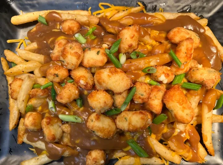 A plate of french fries covered with poutine toppings, fried cheese curds, chives, and gravy.