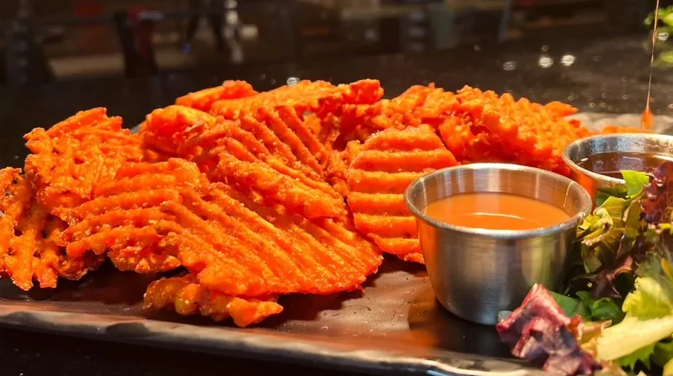 A plate of sweet potato waffle fries along with two cups of dip.